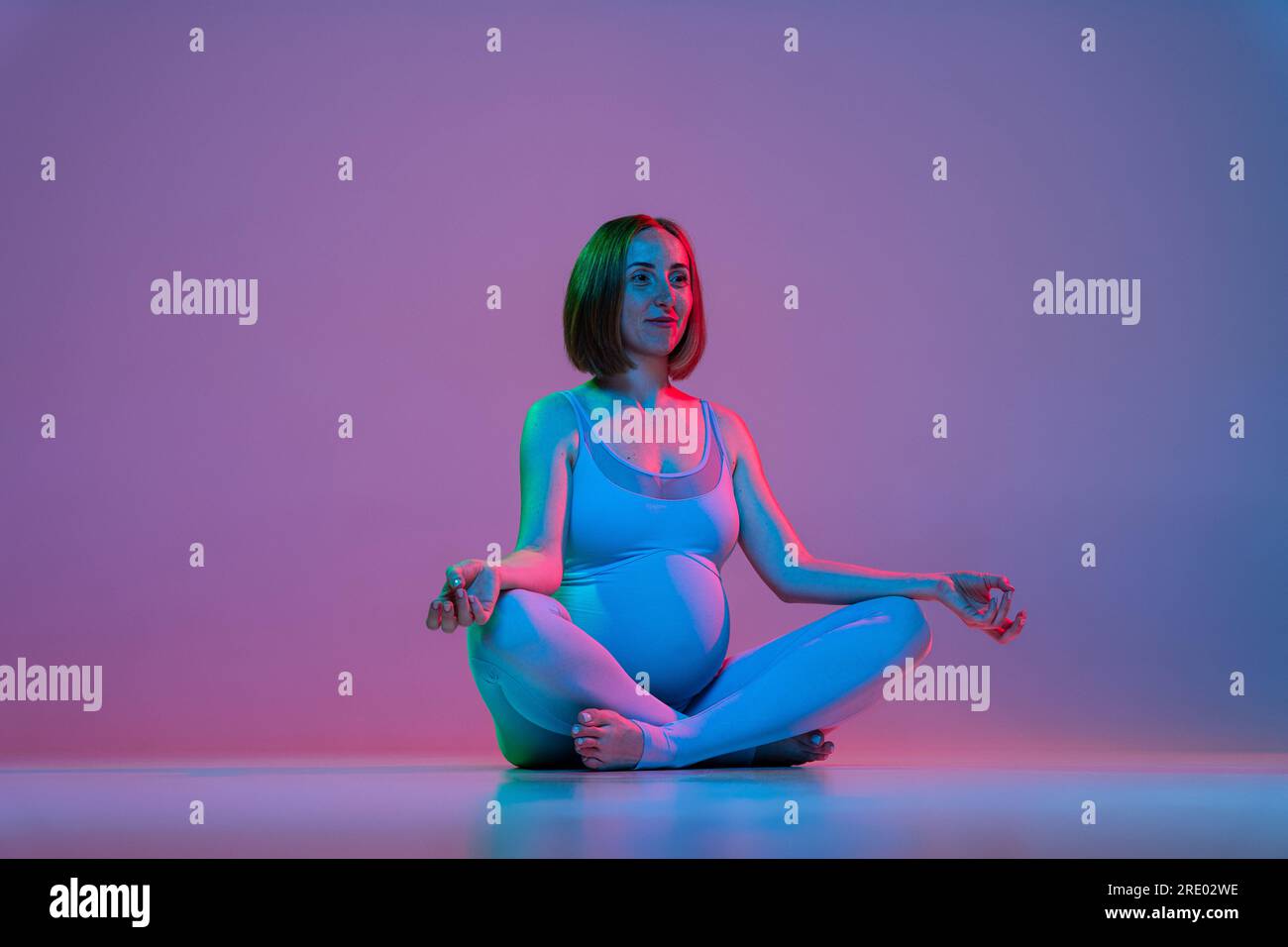 Donna incinta seduta in posa di loto e che fa meditazione al neon Foto Stock