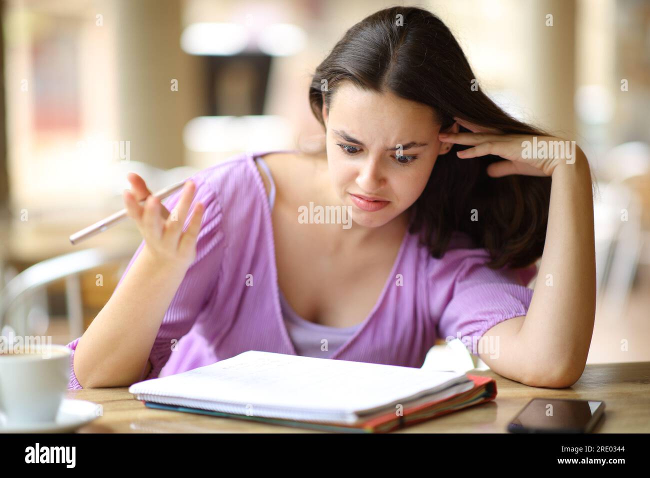 Uno studente perplesso che controlla il notebook seduto in una terrazza bar Foto Stock
