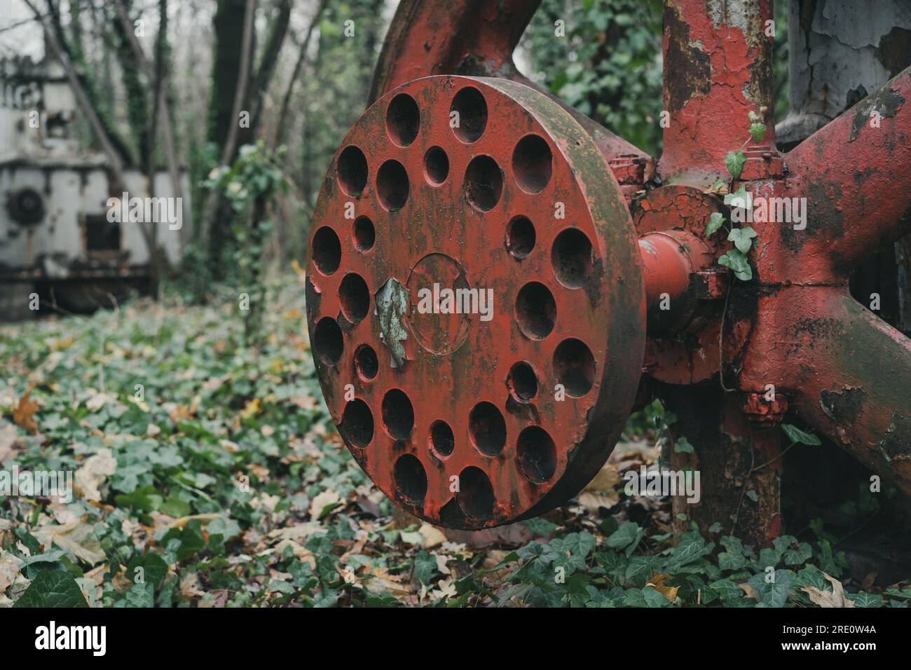 Dettaglio della ruota rossa arrugginita di un vecchio compressore d'aria non utilizzato nella foresta. Macchina per la storia industriale. Produzione di ferro e acciaio. Macchina abbandonata Foto Stock