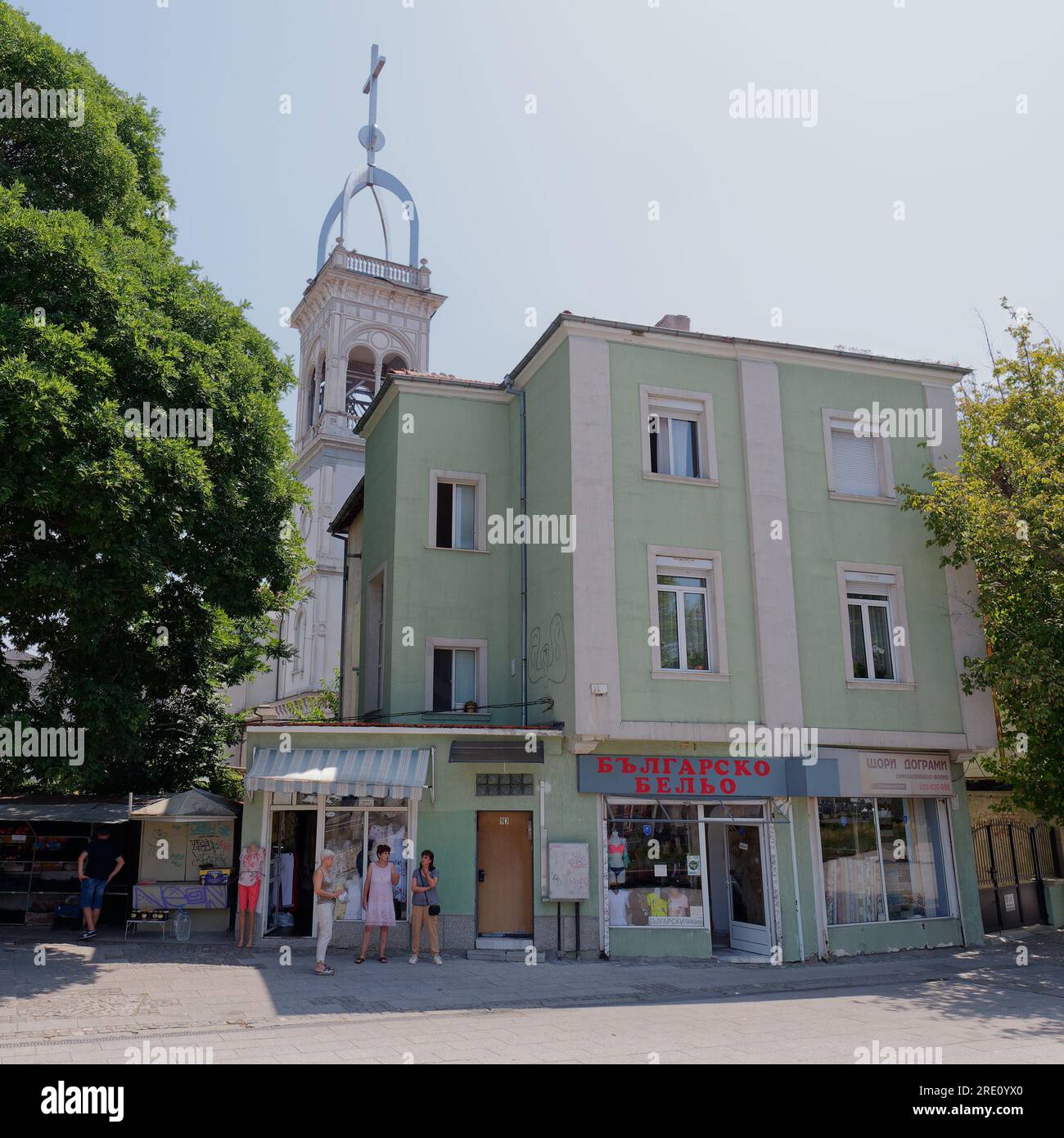 Donne in piedi fuori da un negozio di abbigliamento femminile reso in verde con la torre della chiesa dietro a Plovdiv, Bulgaria Foto Stock