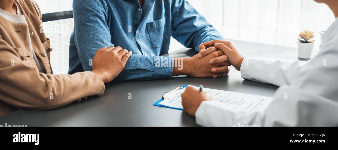 Medico che fornisce consulenza sanitaria compassionevole mentre giovane  coppia paziente che tiene la mano, confortarsi a vicenda dopo rapporto  infertile Foto stock - Alamy