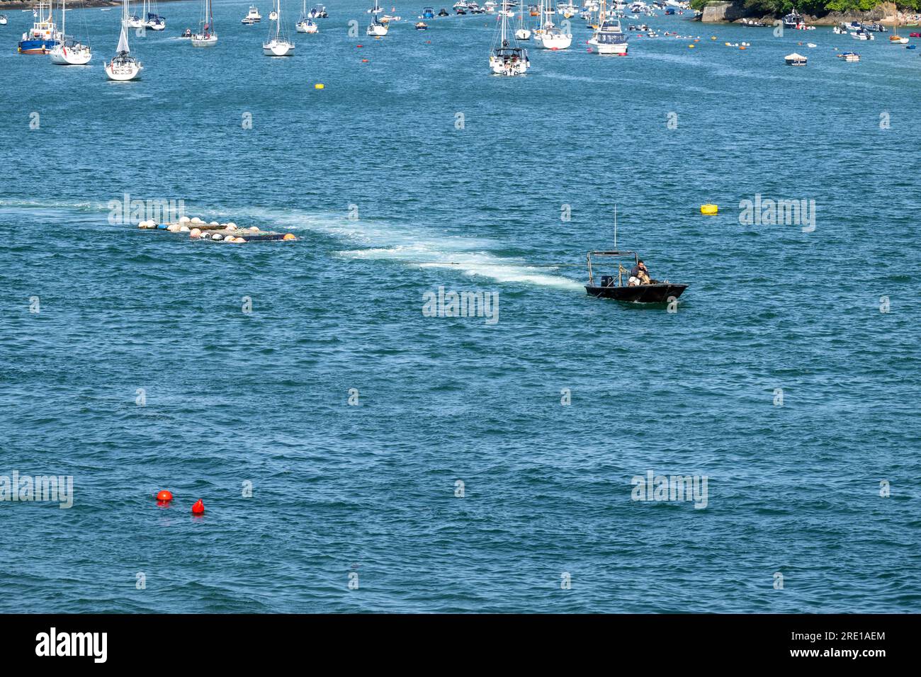 Piccole imbarcazioni costiere che trainano reti di granchio lungo l'estuario di Salcombe in acque calme con yacht mormorati sullo sfondo in un giorno estivo. Foto Stock