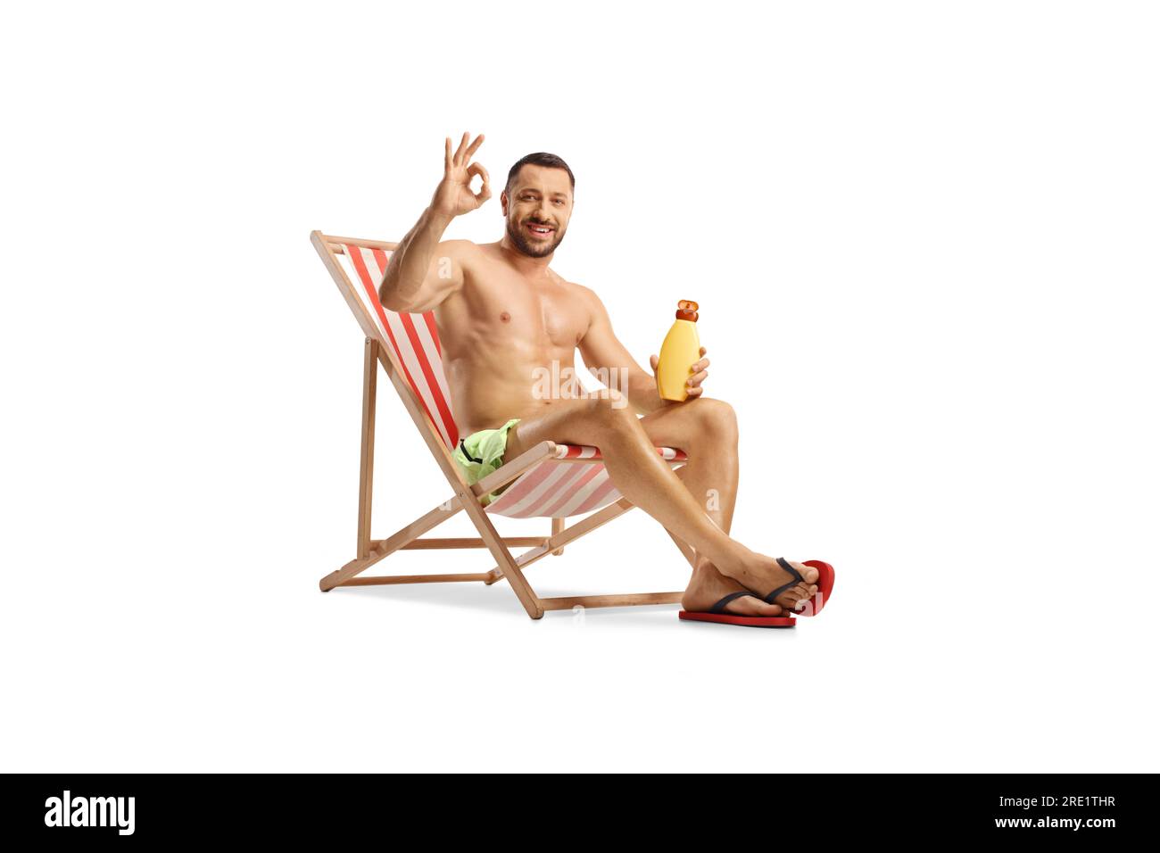 Un giovane seduto su una sdraio che regge una bottiglia di crema solare e un cartello con i gesti ok isolato su sfondo bianco Foto Stock