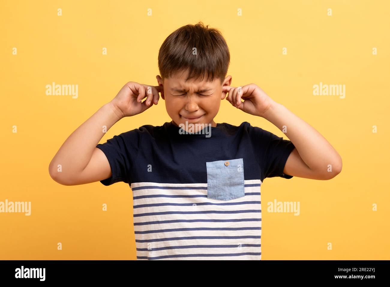 Arrabbiato infelice ragazzo irritato che copre le orecchie isolato su sfondo giallo Foto Stock