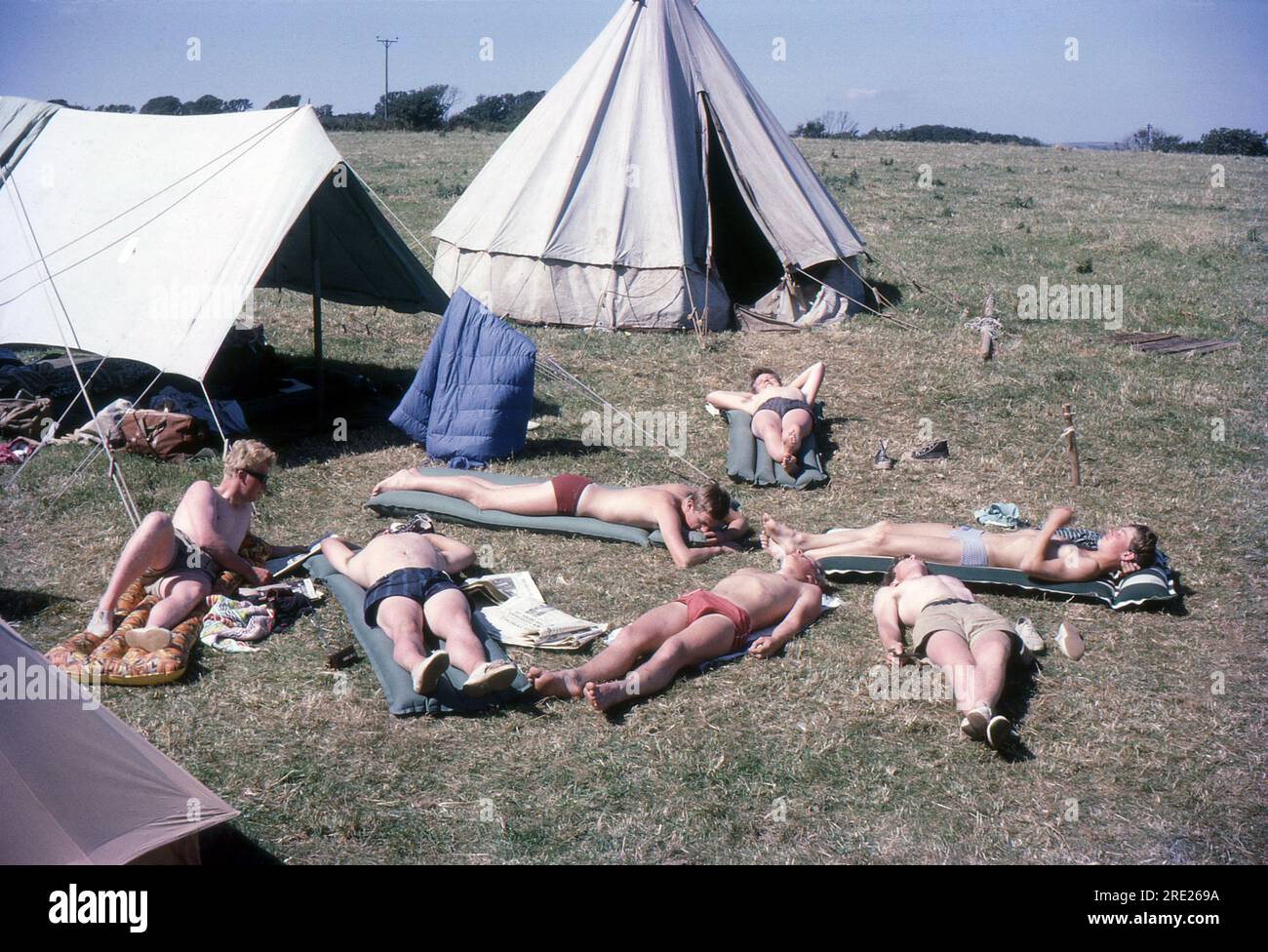 Cornovaglia, Inghilterra. 1964 – Un gruppo di giovani campeggiatori maschi che prendono il sole su materassi gonfiabili. Hanno allestito un campo utilizzando tende dell'esercito britannico in eccedenza in tempo di guerra, tra cui una tenda circolare. Foto Stock