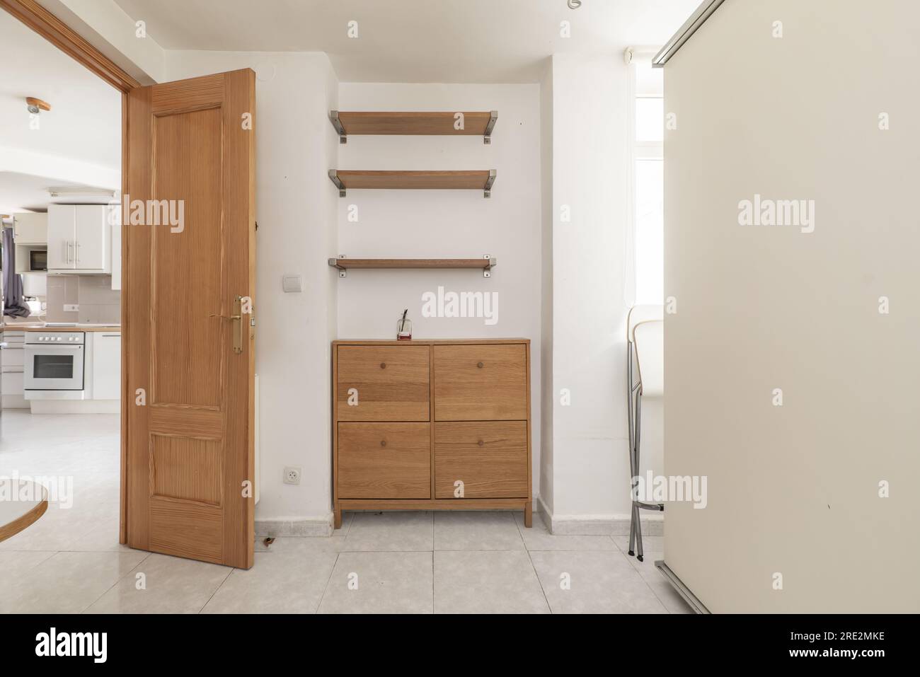 La camera da letto ha una cassettiera con quattro cassetti in legno e tre mensole a muro abbinate, un guardaroba bianco e pavimenti piastrellati Foto Stock