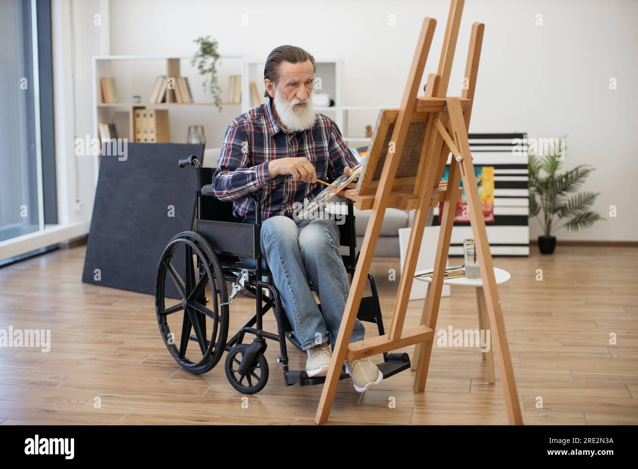 Ritratto di un uomo anziano felice in pensione trovando ispirazione e disegnando foto su tela con acquerelli. Uomo carismatico anziano con disabilità dr Foto Stock