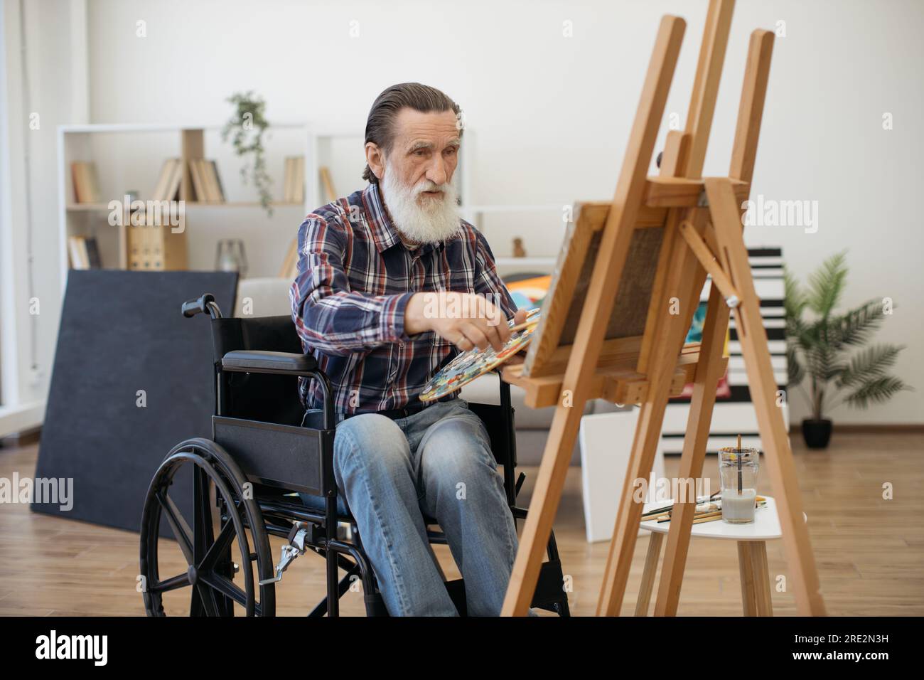 Ritratto di un uomo anziano felice in pensione trovando ispirazione e disegnando foto su tela con acquerelli. Uomo carismatico anziano con disabilità dr Foto Stock