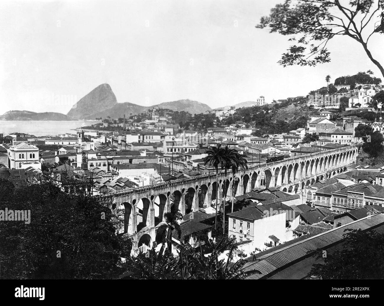 Rio de Janeiro, Brasile: c. 1925 Una vista di Rio de Janeiro con il picco del Pan di zucchero nel porto e l'Old Aquaduct in primo piano. L'acquedotto utilizzato per rifornire la città di acqua, ut è ora utilizzato come viadotto da una compagnia di tram. Foto Stock