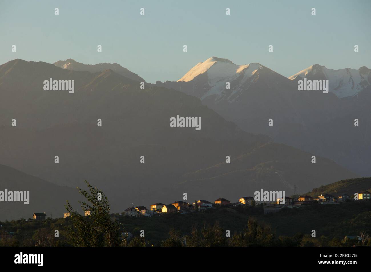 Le montagne innevate dietro una fila di case private sul pendio, illuminate dal sole mattutino di colore arancione. Foto Stock
