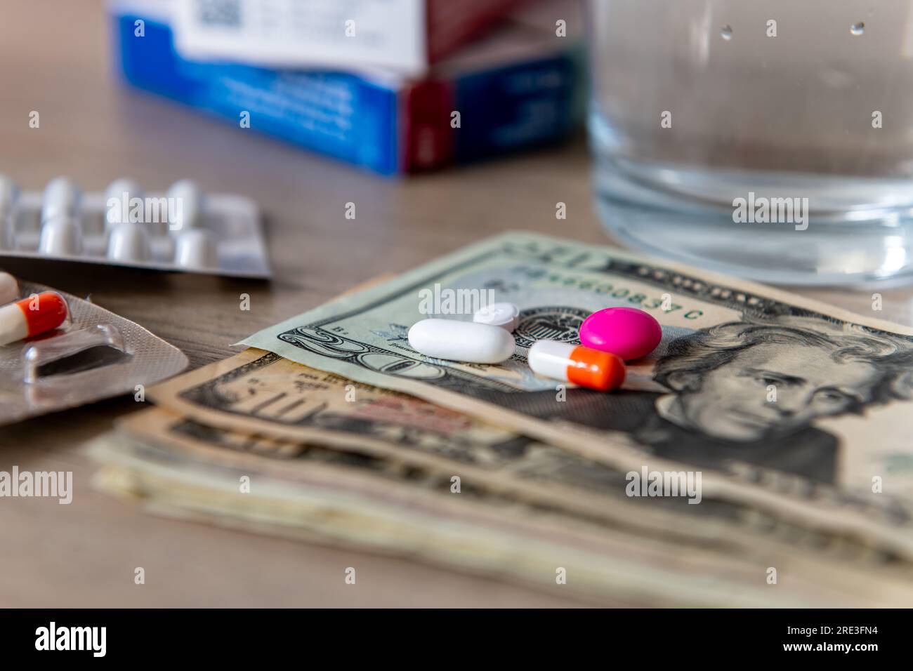 Un concetto di costo medico con un bicchiere d'acqua, varie medicine e banconote in dollari americani. Foto Stock