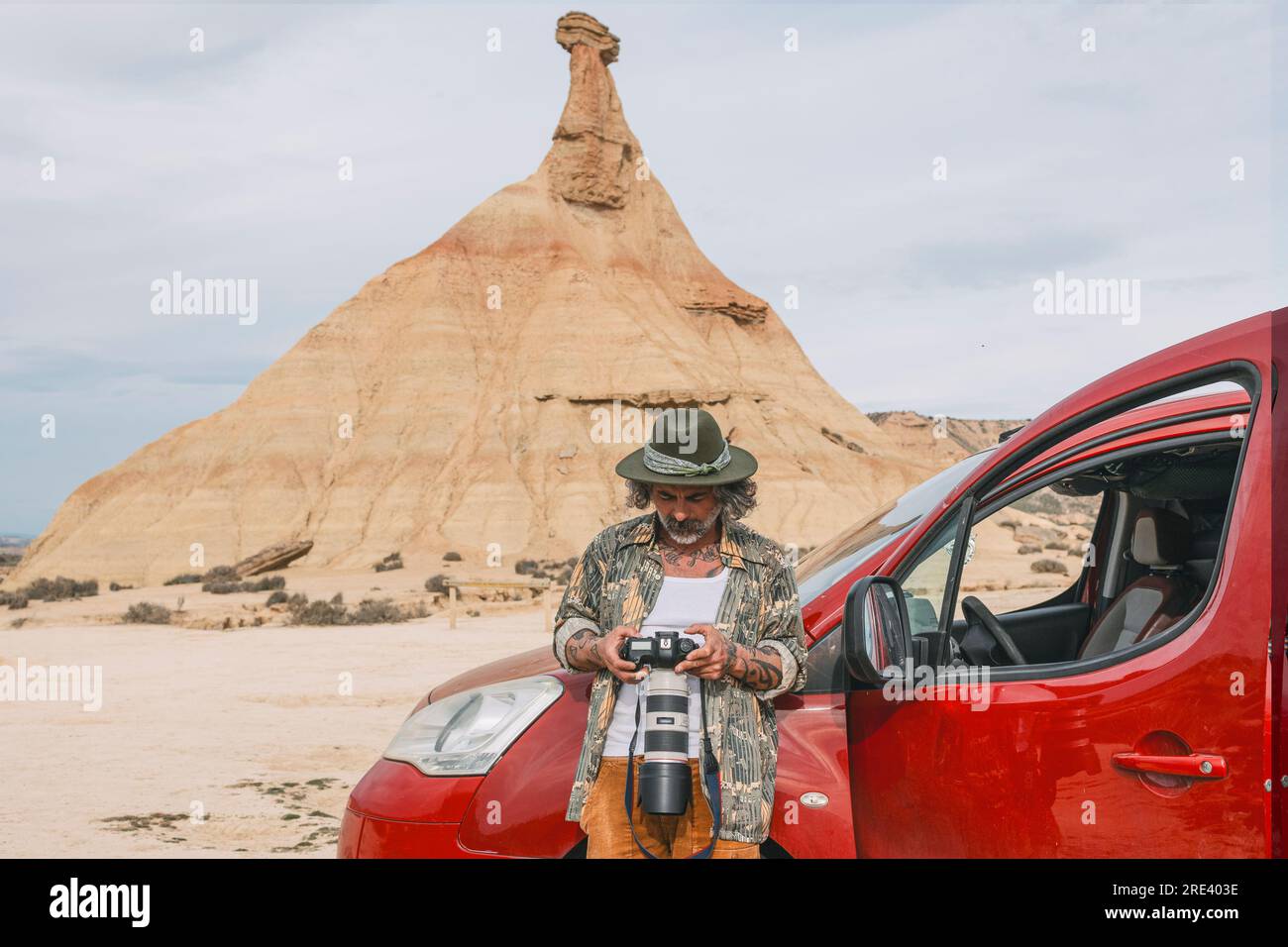 Viaggiatore di mezza età che guarda le foto con una fotocamera reflex nel paesaggio desertico delle Bardenas Reales, Arguedas, Navarra, Spagna Foto Stock