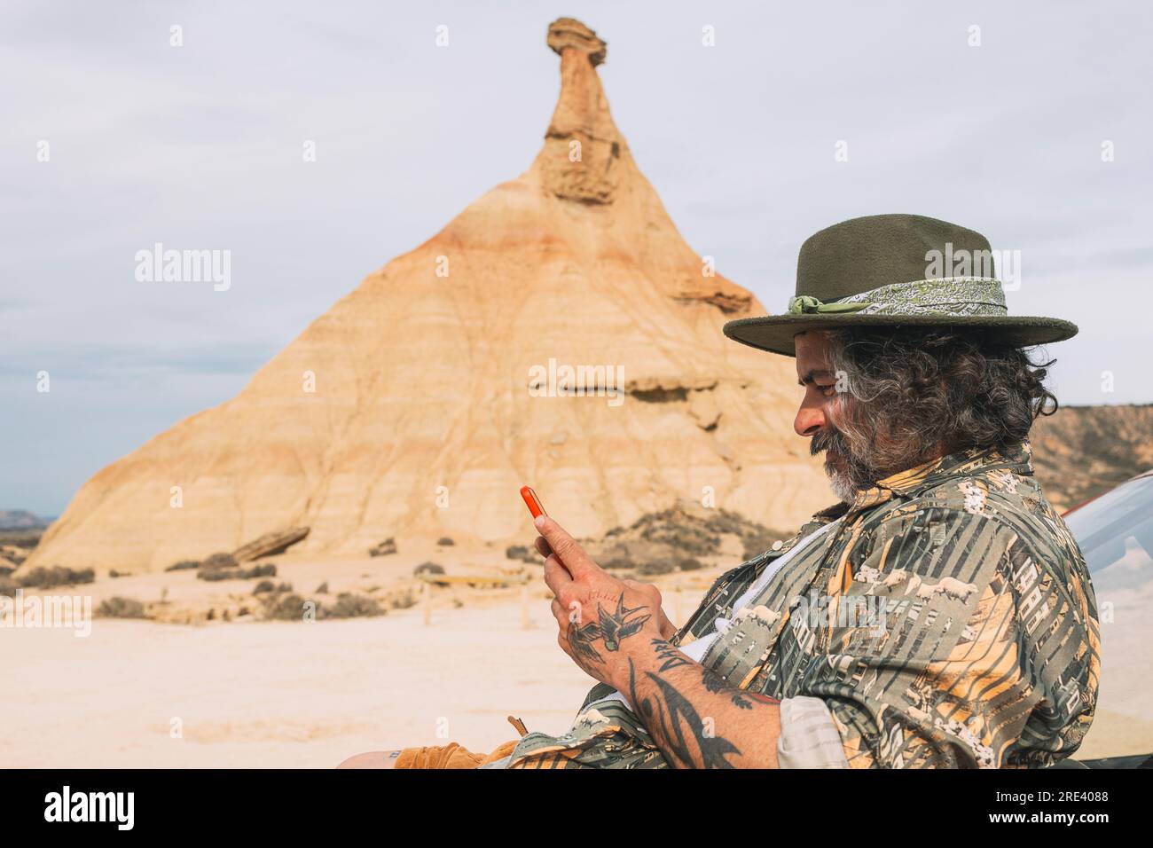 Viaggiatore che guarda il cellulare nel paesaggio desertico di Bardenas Reales, Arguedas, Navarra, Spagna Foto Stock