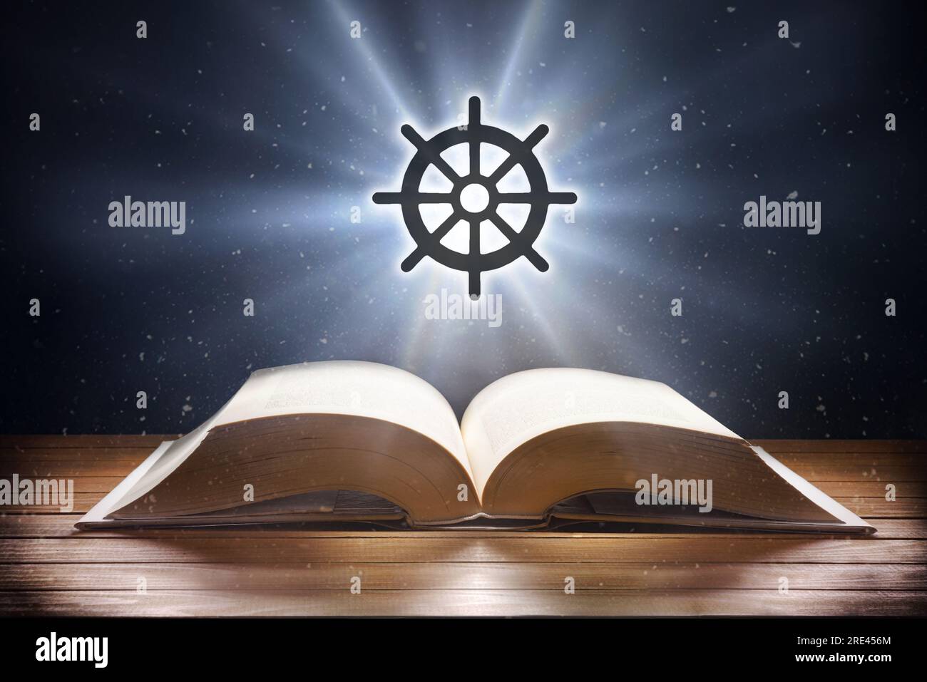 Libro aperto su tavolo di legno e simbolo buddista con fascio di luce su sfondo scuro. Vista frontale. Foto Stock