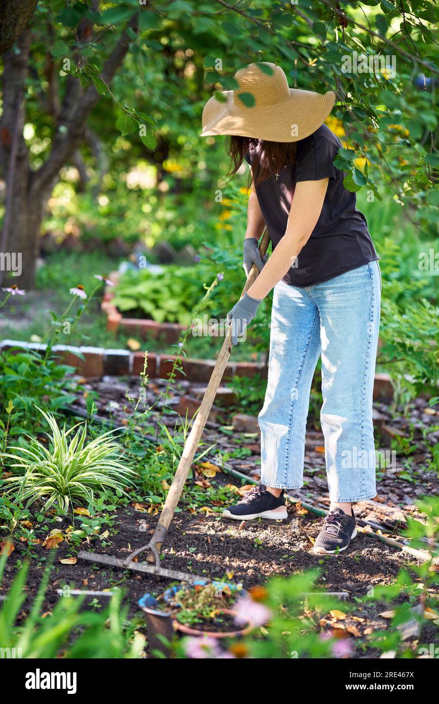 Donna giardiniera in cappello e guanti protettivi che scavano terreno con  rastrello nel suo giardino. Lavori di giardinaggio Foto stock - Alamy