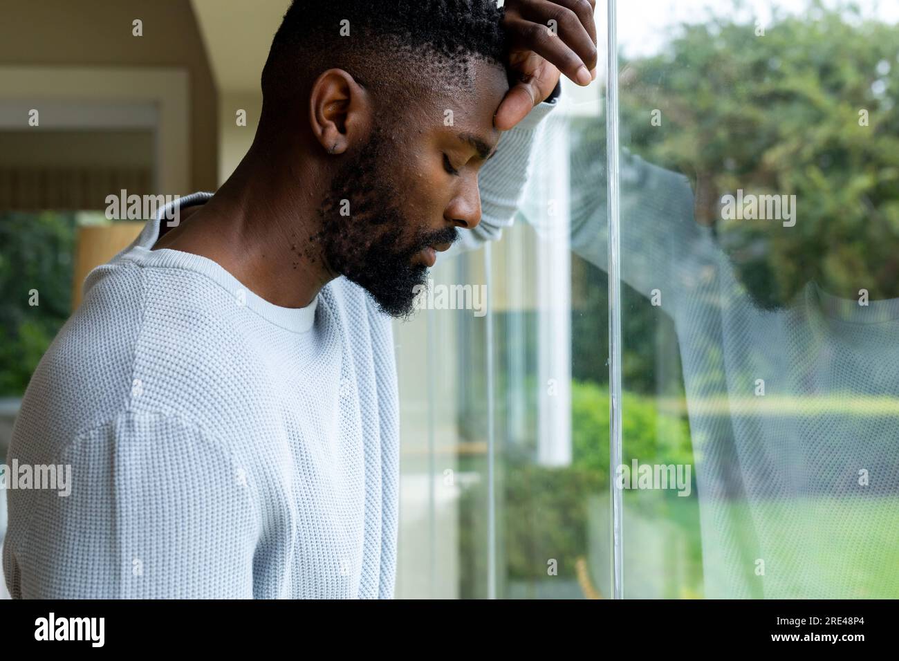 Un uomo afro-americano premuroso che si appoggia alla finestra di casa Foto Stock