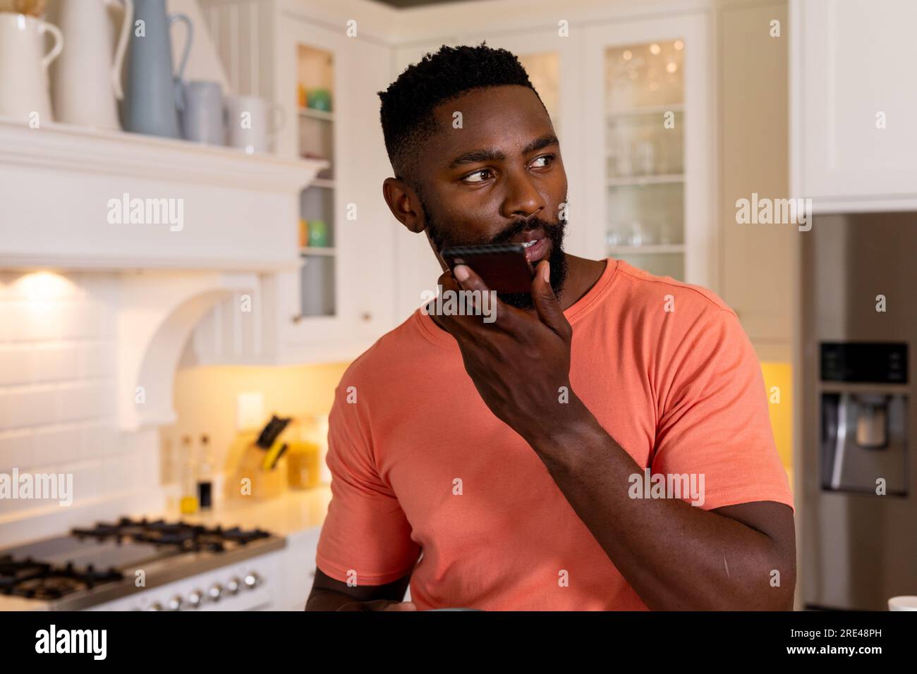 Uomo afro-americano che parla su smartphone in cucina bianca Foto Stock