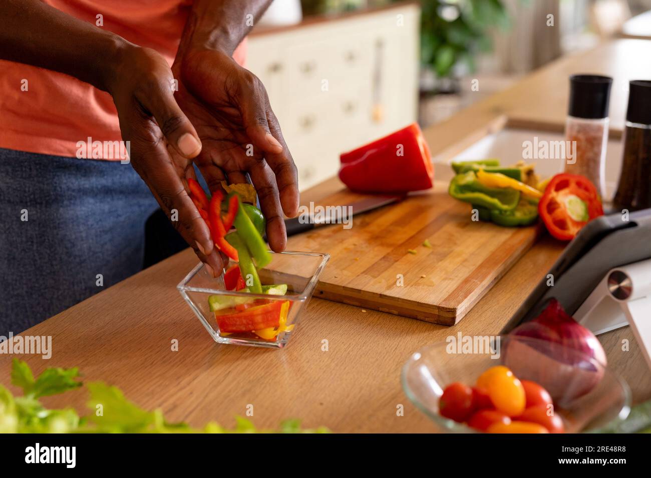 Mani di un uomo afroamericano che prepara il pasto usando un tablet in cucina Foto Stock