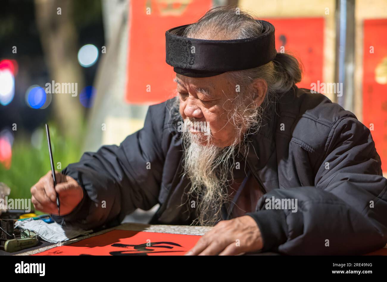 Un anziano vietnamita con una lunga barba magra dipinge la calligrafia di carattere cinese per raccogliere fondi vicino al lago Hoan Kiem nel centro di Hnaoi, in Vietnam Foto Stock