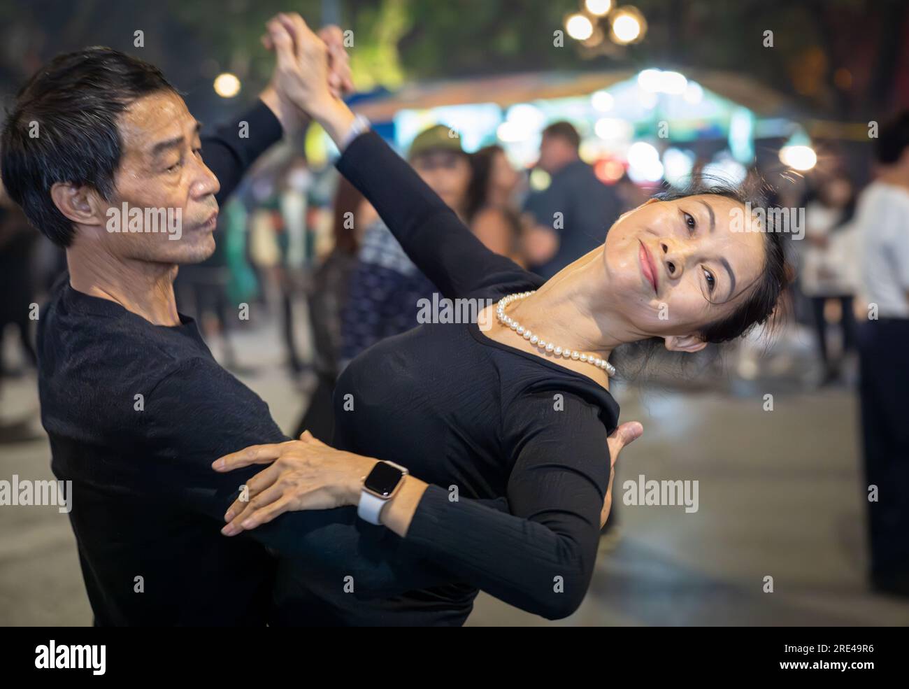 Una coppia vietnamita di mezza età vestita di danza nera per le strade di notte accanto al lago Hoan Kiem nel centro di Hanoi, in Vietnam. Foto Stock