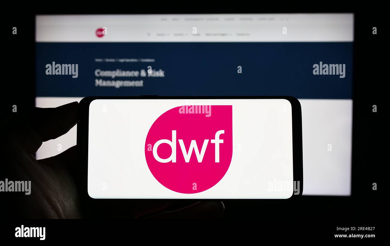 Persona in possesso di un cellulare con il logo della società legale britannica DWF Group plc sullo schermo davanti alla pagina Web aziendale. Concentrarsi sul display del telefono. Foto Stock