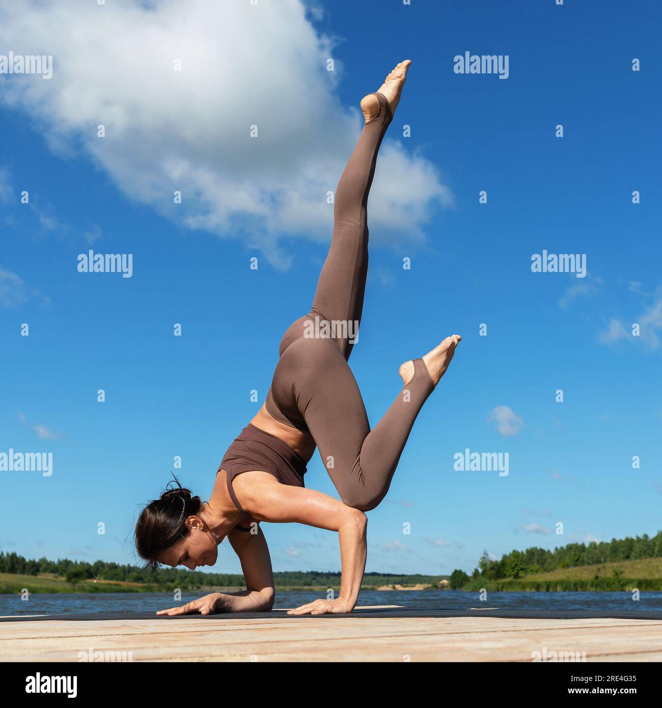 Una donna che pratica yoga, esegue l'esercizio Eka Pada Bakasana, la posa di una gru con una gamba allungata, si allena in abbigliamento sportivo mentre si sta in piedi su Foto Stock