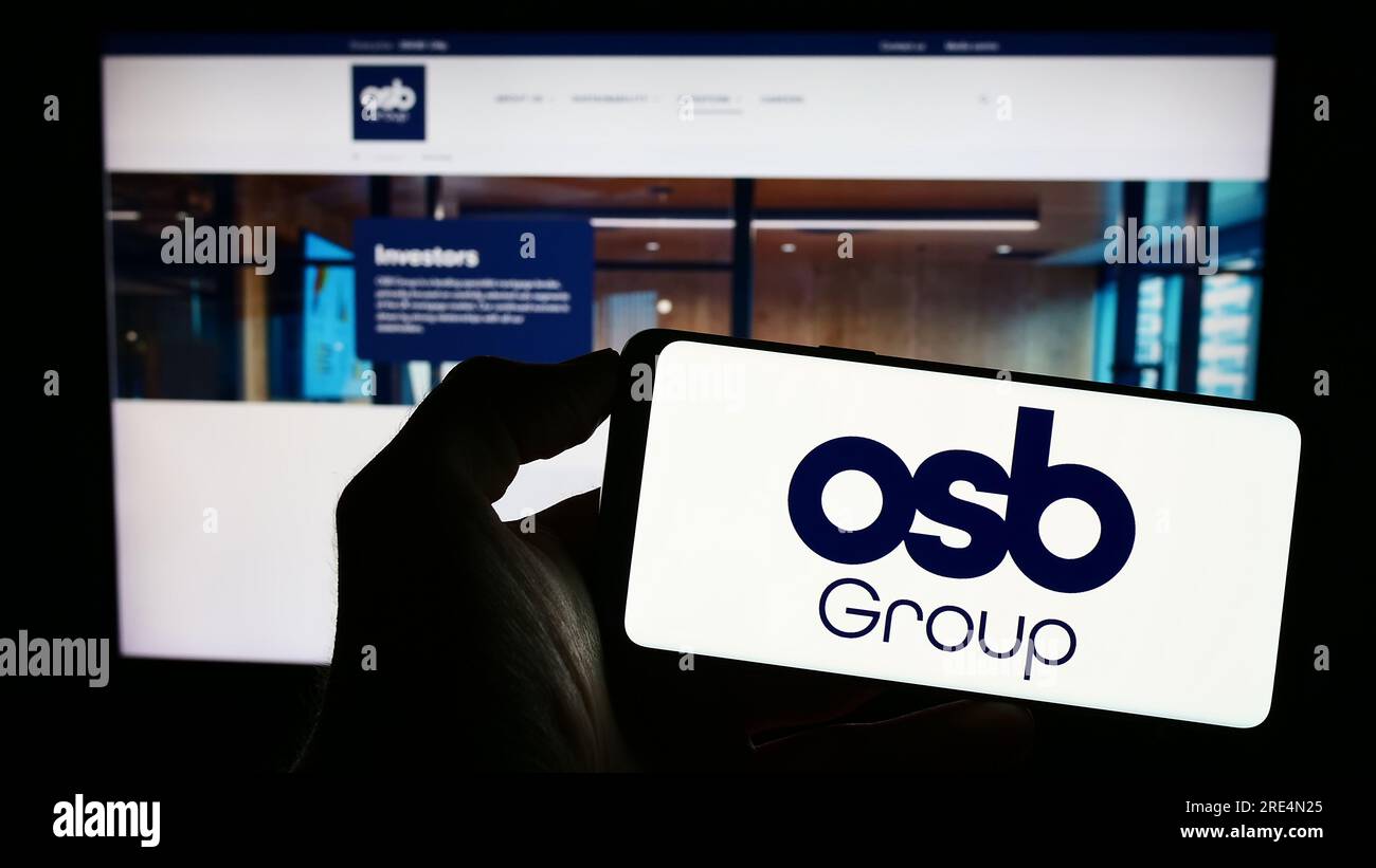 Persona in possesso di un cellulare con il logo della società finanziaria britannica OSB Group plc sullo schermo davanti alla pagina Web aziendale. Concentrarsi sul display del telefono. Foto Stock