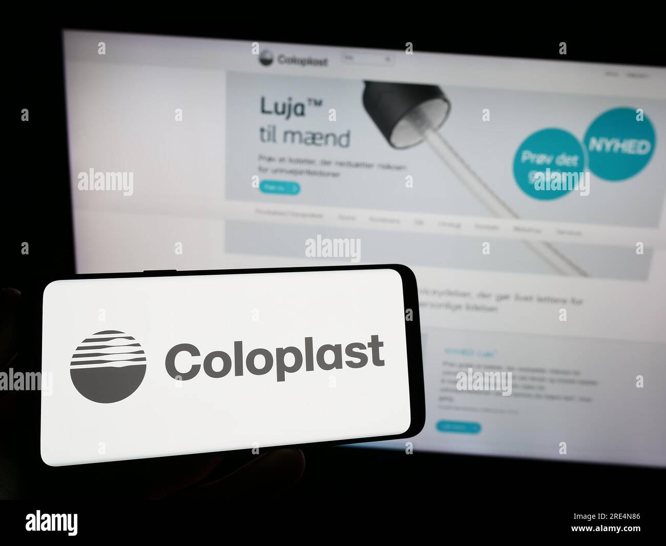 Persona in possesso di smartphone con logo della società sanitaria danese Coloplast COME sullo schermo di fronte al sito web. Concentrarsi sul display del telefono. Foto Stock