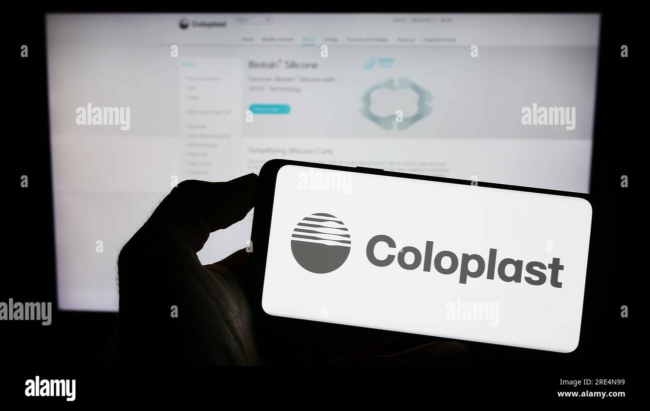 Persona in possesso di cellulare con logo della società sanitaria danese Coloplast COME sullo schermo di fronte alla pagina Web aziendale. Concentrarsi sul display del telefono. Foto Stock