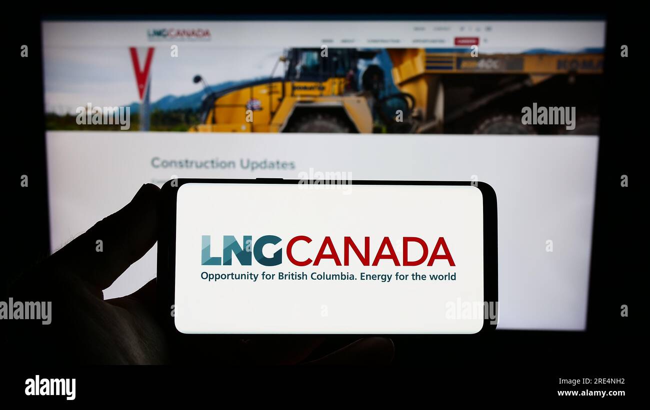 Persona che possiede uno smartphone con il logo del progetto di energia industriale LNG Canada sullo schermo di fronte al sito Web. Concentrarsi sul display del telefono. Foto Stock