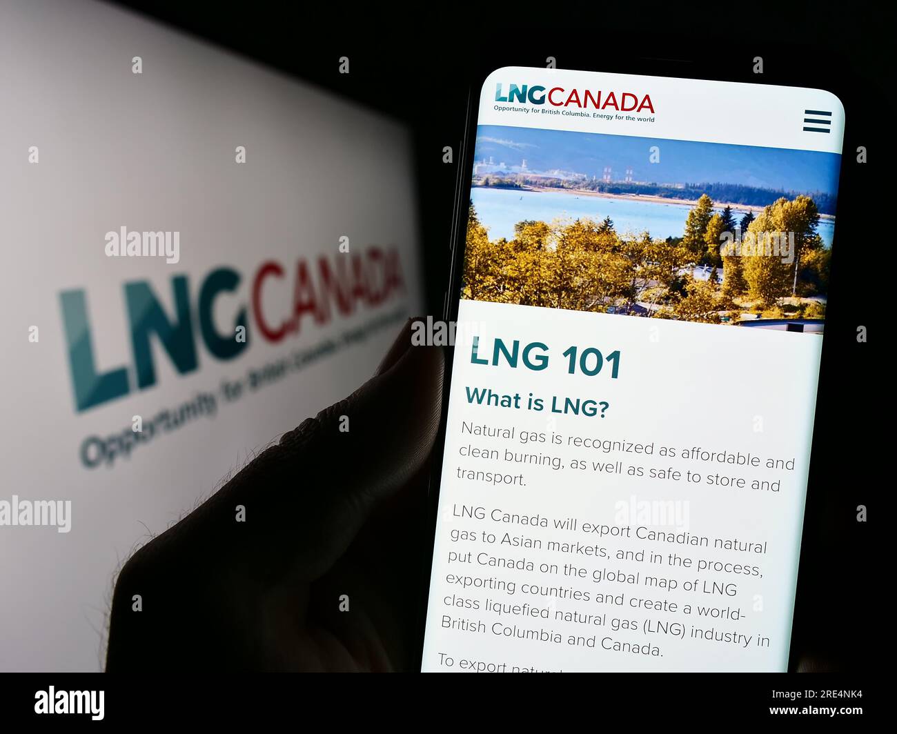 Persona che tiene il cellulare con il sito Web del progetto di energia industriale LNG Canada sullo schermo davanti al logo. Concentrarsi sul centro del display del telefono. Foto Stock