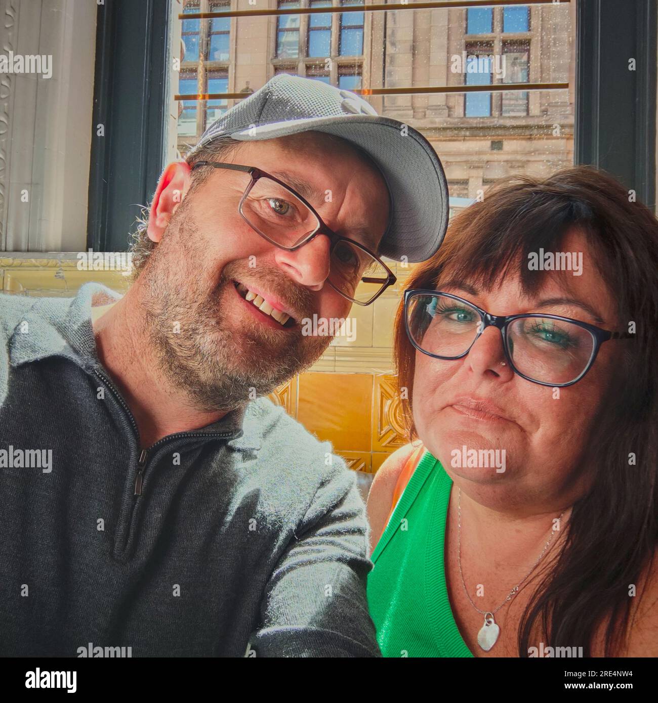 La coppia di mezza età con gli occhiali seduti in una casa pubblica sorridente davanti alla fotocamera.il modello è disponibile se necessario. Foto Stock