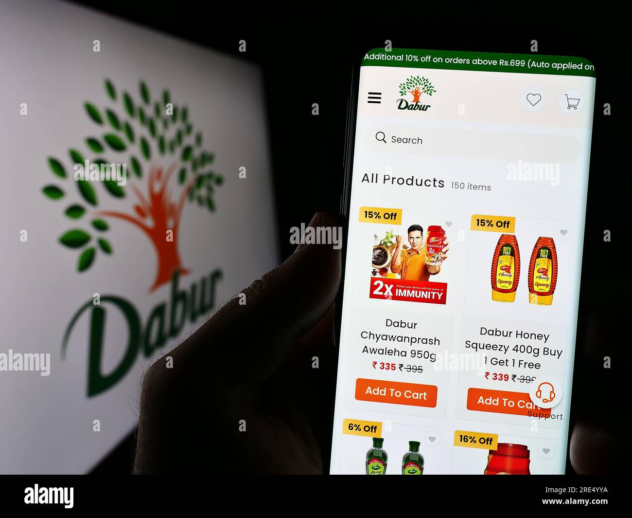 Persona che possiede il cellulare con la pagina Web dell'azienda Ayurveda Dabur India Limited sullo schermo davanti al logo. Concentrarsi sul centro del display del telefono. Foto Stock