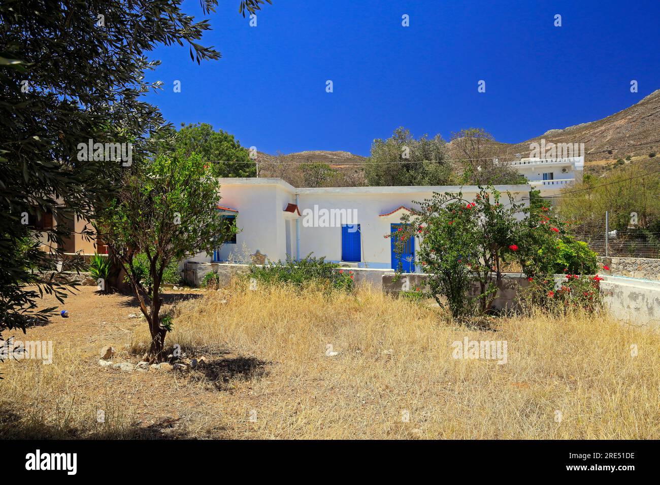 Casa e giardino di stile tradizionale, imbiancati con porte e finestre blu. Isola di Tilos, vicino a Rodi, Dodecaneso, Grecia Foto Stock