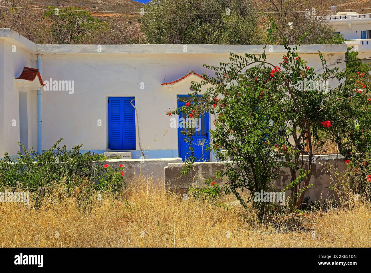 Casa e giardino di stile tradizionale, imbiancati con porte e finestre blu. Isola di Tilos, vicino a Rodi, Dodecaneso, Grecia Foto Stock