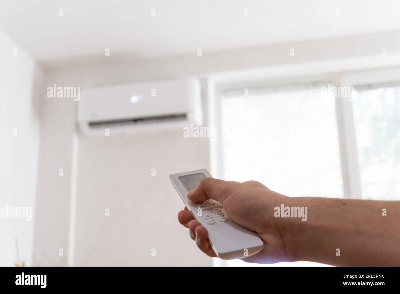 Comando a distanza manuale rivolto verso il climatizzatore. Giovane uomo che accende il condizionatore d'aria con telecomando. Aumento delle temperature con temperature elevate. Foto Stock