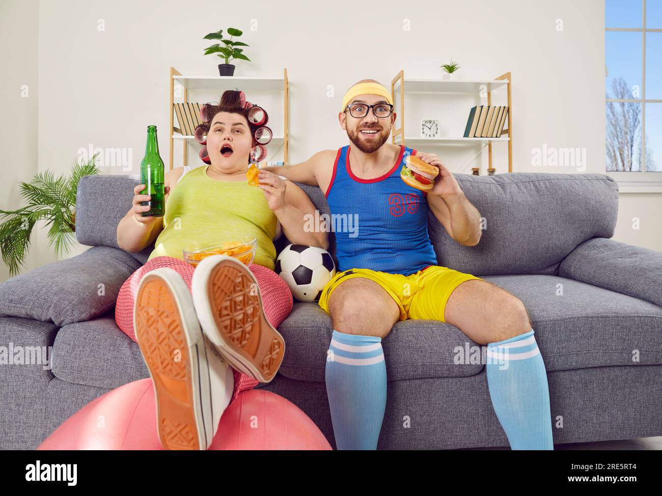 Una divertente coppia di famiglie che si divertono a imbrogliare, mangiano cibo spazzatura e guardano il calcio in TV Foto Stock