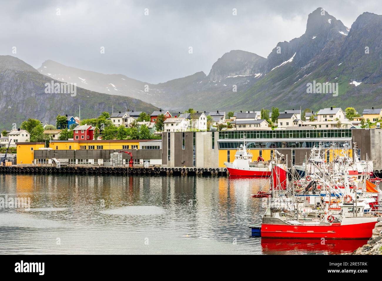 Barche da pesca al molo con case e montagne sullo sfondo al villaggio di Husoy, isola di Senja, Norvegia Foto Stock