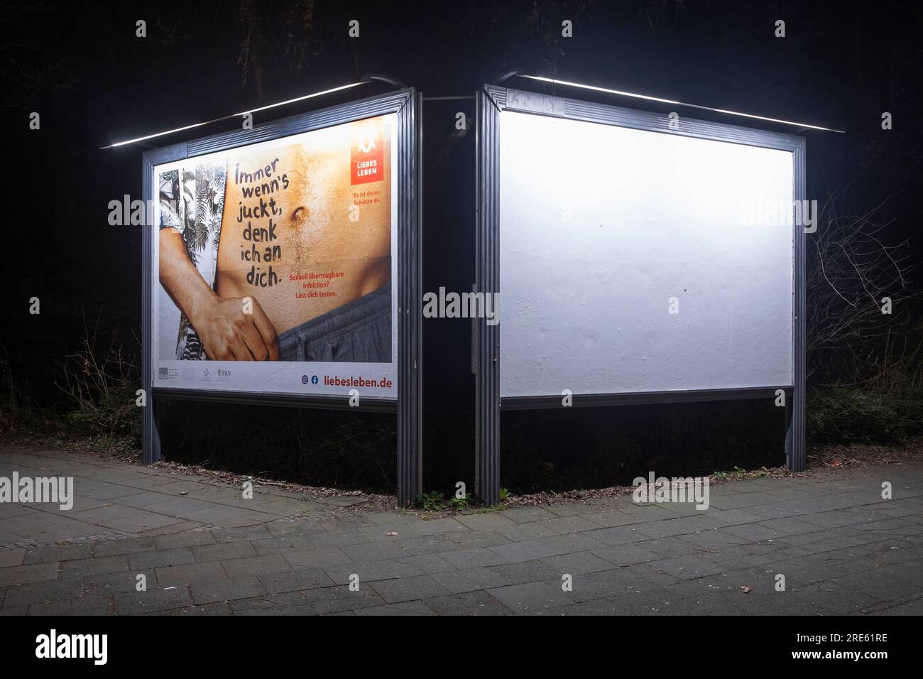 Due cartelloni illuminati di notte. Uno avverte di malattie veneree, l'altro è vuoto. Foto Stock
