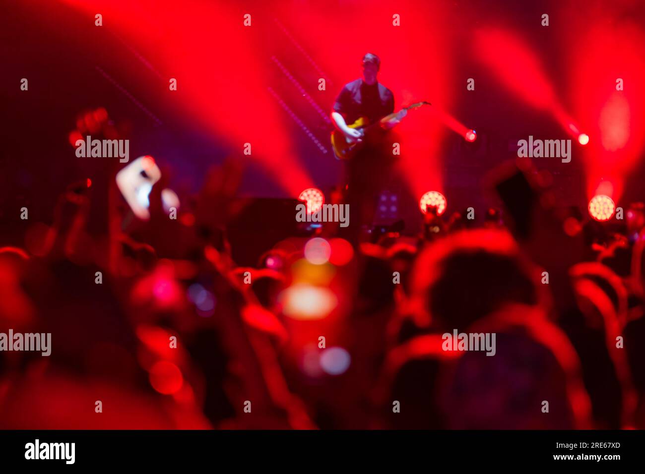 Folla di persone che si radunano intorno al palco e ascoltano il cantante che suona strumenti musicali durante le esibizioni con luci al neon rosse durante il concerto Foto Stock