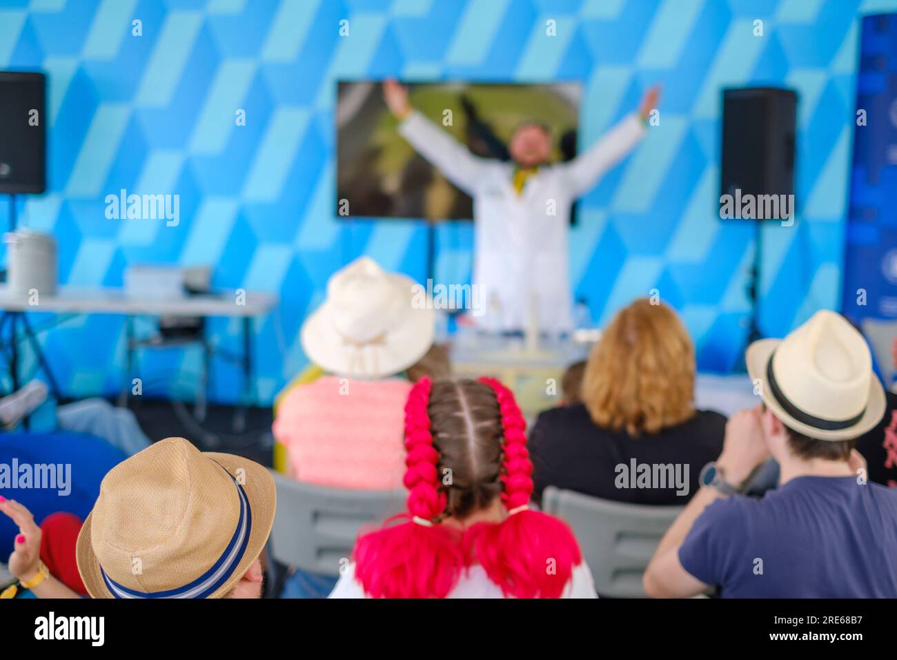 Vista posteriore degli adolescenti moderni che guardano i trucchi dello spettacolo dell'uomo che si esibisce al tavolo durante l'evento Foto Stock