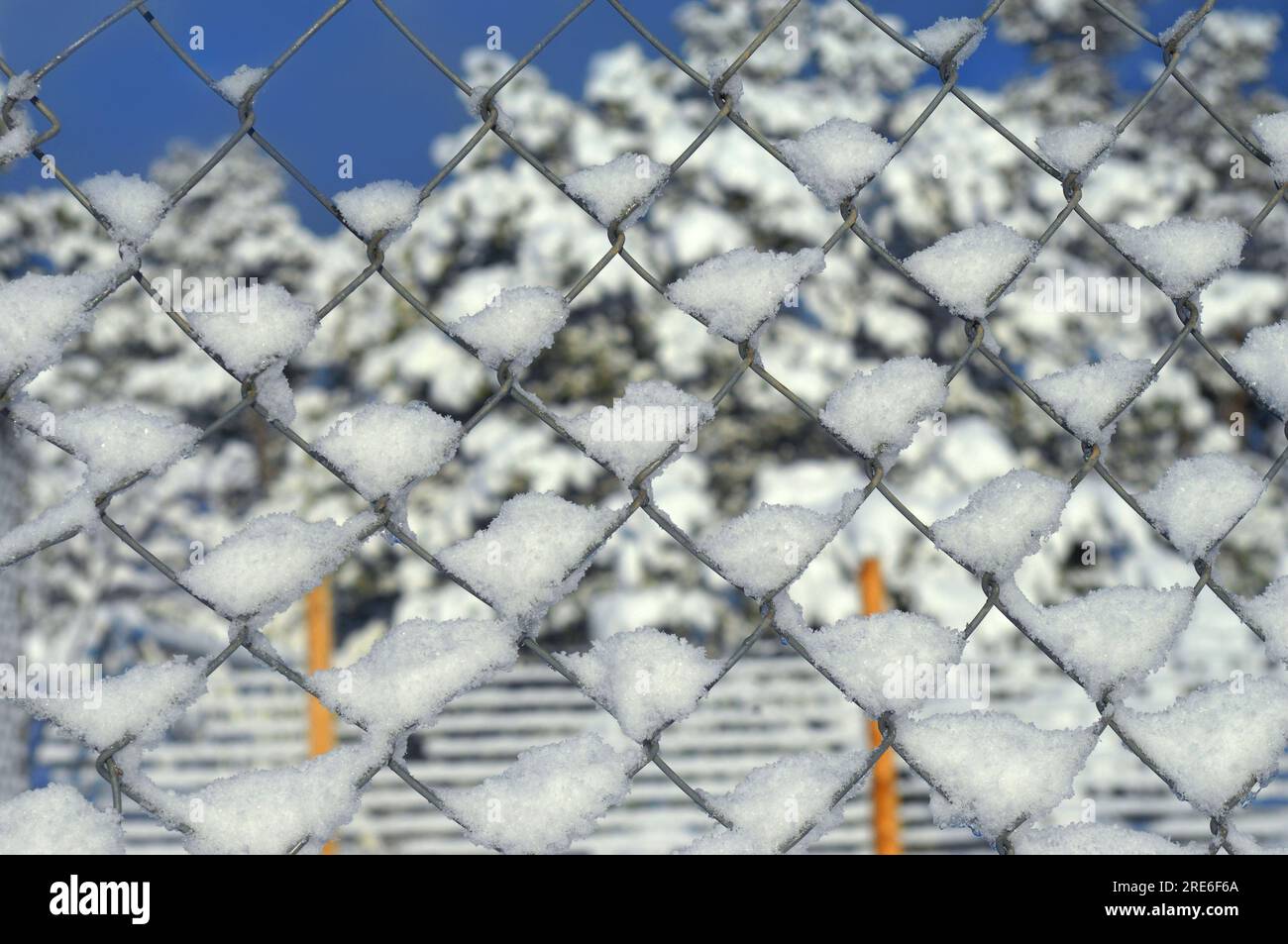 Immagine di sfondo di neve attaccata a una recinzione a catena. Cime blu del cielo sullo sfondo. Foto Stock