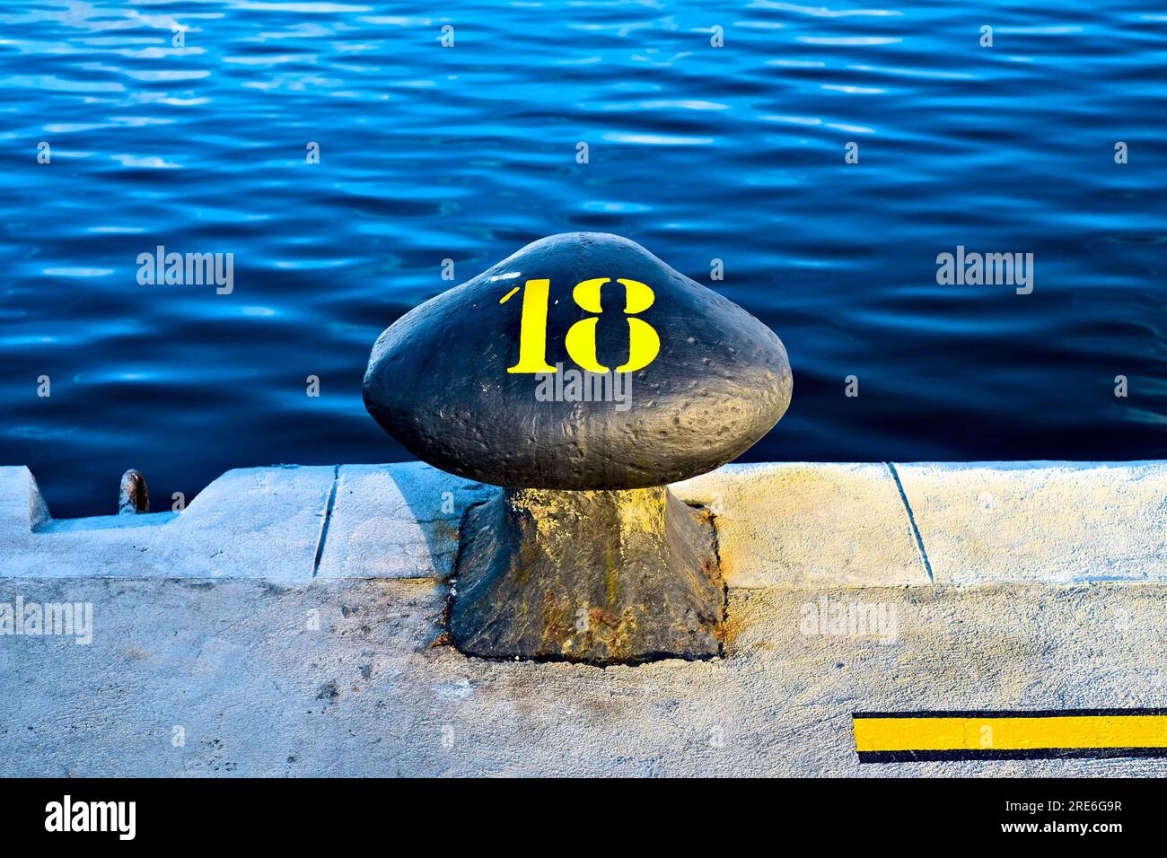 Numero 18, diciotto, cifra stencil gialla dipinta su un grande dissuasore commerciale al bordo di un bacino portuale. Foto Stock