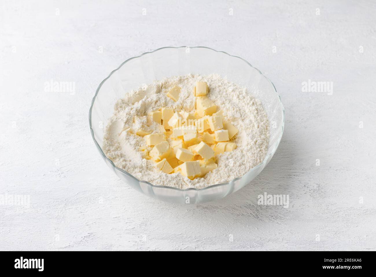 Recipiente di vetro con cubetti di farina e burro su sfondo grigio chiaro. Cucinare deliziose torte fatte in casa passo dopo passo. Foto Stock