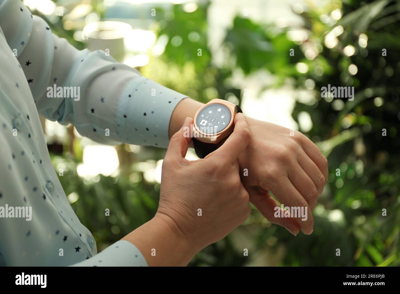 Donna che imposta il sistema di controllo della casa intelligente tramite smartwatch all'aperto, primo piano. Interfaccia app con icone sul display Foto Stock