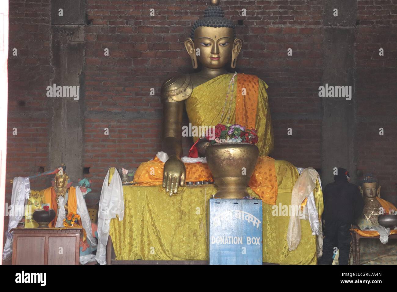 Statua del Buddha realizzata in bronzo, con sfondo murato e decorata con tessuti colorati Foto Stock