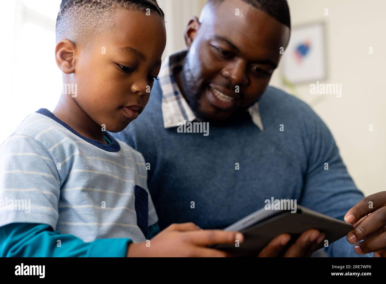 Padre e figlio afro-americani felici seduti in salotto a casa usando un tablet insieme Foto Stock