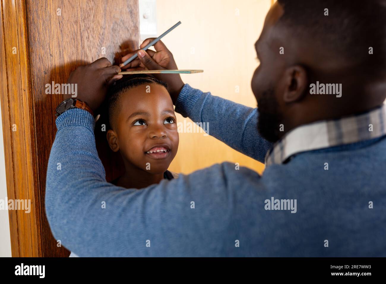 Padre afro-americano felice che misura il figlio e l'altezza di marcatura sul telaio della porta a casa Foto Stock