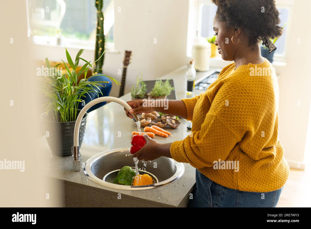 Donna afro-americana più grande che risciacqua verdure in cucina Foto Stock