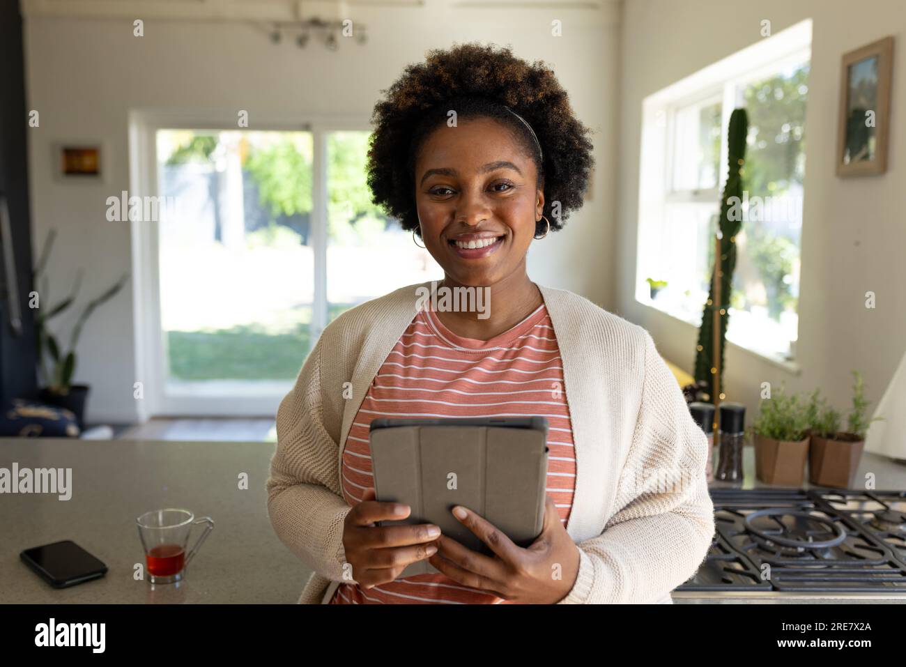 Ritratto di una donna afroamericana felice e di taglia più grande che tiene un tablet in cucina Foto Stock